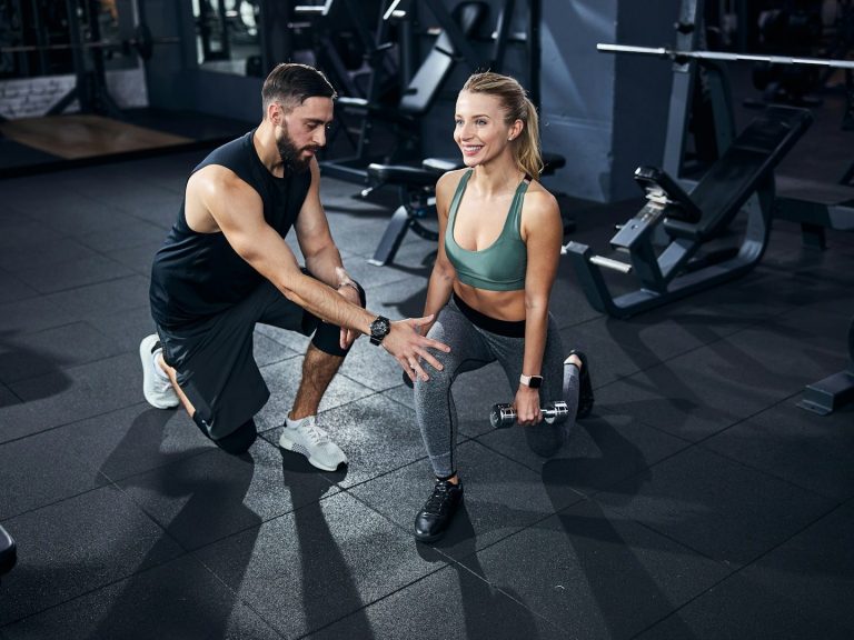 Ein Trainer unterstützt eine Frau beim Ausführen von Lunges im Fitnessstudio.