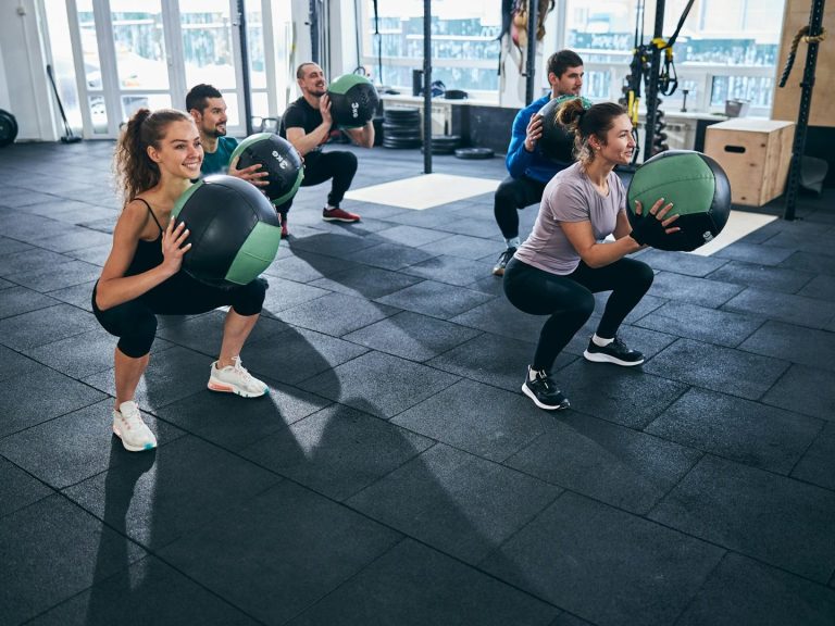 Gruppentraining mit mehreren Personen, die Medizinbälle im Fitnessstudio heben.